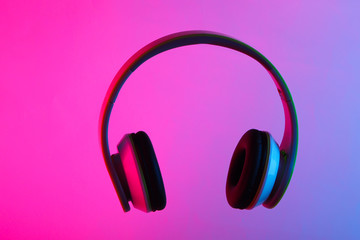 Modern stereo headphones with neon vibrant pink blue light. Gradient glow.