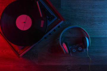 Stereo headphones and retro vinyl record player on a wooden floor with blue-red neon light....