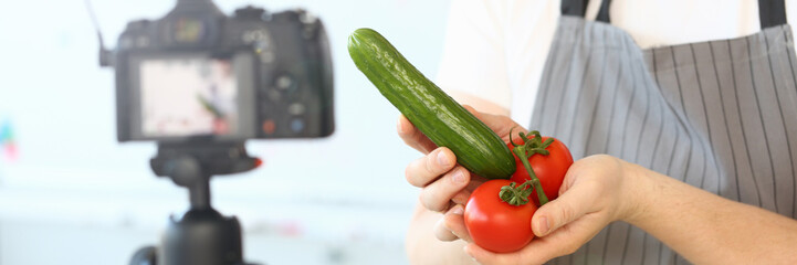 Comic Culinary Blogger Holding Organic Vegetables. Chef Recording Joke with Cucumber and Tomato for Blog on Camera. Man in Apron Showing Ingredient Assortment for Healthy Food Horizontal Shot.