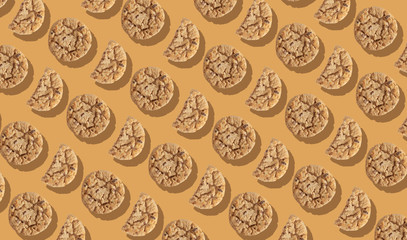A pattern of a large number of light crumbly cookies with chocolate chips on an orange background illuminated by hard light.