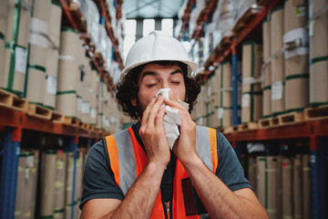 Young sick african warehouse worker blowing nose while working wearing safety vest