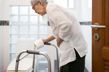 Senior woman with diarrhea holding tissue roll near a toilet bowl,elderly have abdominal...