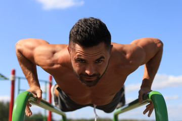 Strong sporty man holding plank on bars outdoors. Work out