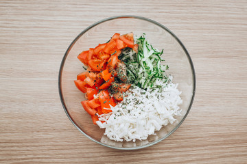 Transparent glass salad bowl on a wooden background, it contains tomatoes cucumbers and cabbage, top view. Good nutrition