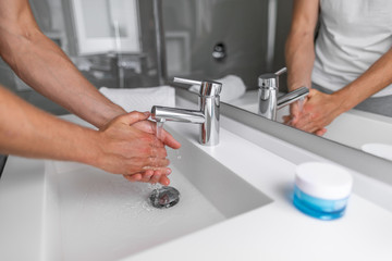 Man washing hands in hot water bathroom faucet sink running water for clean wash.