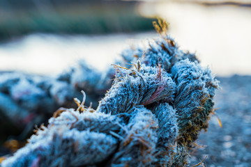 Thick rope covered in ice from a heavy frost in winter, diiscarded next to the Thames in Essex, England