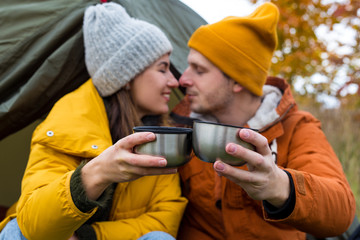 travel, trekking and hiking concept - portrait of cute couple drinking tea near green tent in autumn forest