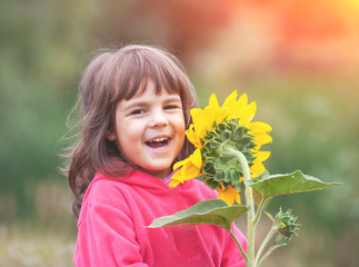 Happy laughing little girl with sunflower outdoors in summer