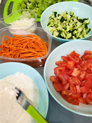 Sliced tomatoes and cucumbers spread out on a thin pita bread. Preparations for Shawarma in different plates on the kitchen table at home.