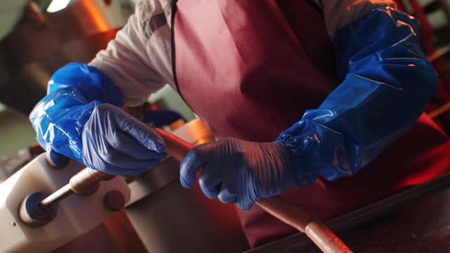 woman employee pulls string of sausages from machine in shop