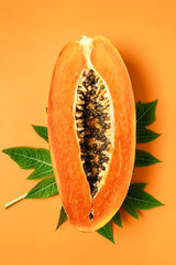 Ripe freshly cut papaya fruit with green papaya leaf on orange background, flat lay, vertical composition