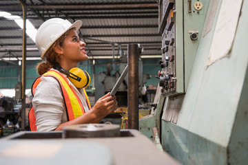 Female industrial worker working and checking machine in a large industrial factory with many equipment.