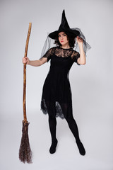 beautiful woman in black witch halloween costume with broom over white background