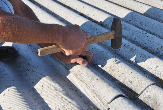 A Building Contructor Is Nailing The Asbestos Roof Tile With A Hammer.