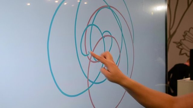 Girl draws with her finger different colored spiral lines on a large touch