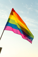 Gay rainbow flag on a sunny summer day with blue sky. Mediterranean sea cost with cliffs.