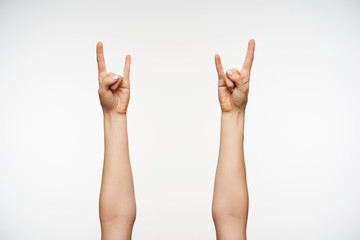 Close-up of young woman's hands showing heavy metal and rock gesture while posing against white background. Body language and signs concept