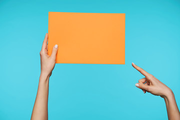 Pretty woman's hand keeping orange paper in one hand and pointing on it with forefinger of another...