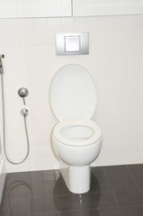 A wall mounted, built-in white toilet on the marbled black floor with a chrome bidet spray shower aside.
