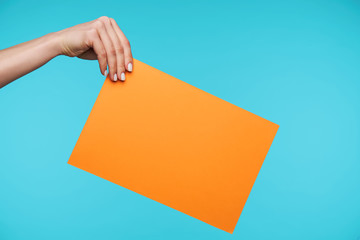 Young secretary with white manicure keeping her hand raised while holding orange envelope with important documents while standing over blue background
