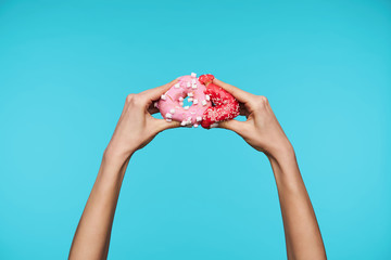 Indoor shot of pretty woman's hands being raised while posing blue background, imitating like pac-man donut eating another donut. Hands and gesturing concept