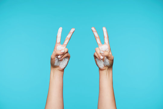 Studio shot of lady's stained hands being raised while showing letter V in sign language hand symbol viewed from back, isolated over blue background