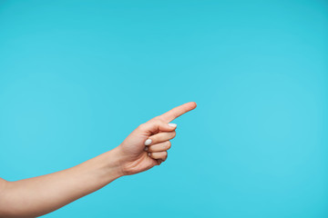 Horizontal photo of raised lady's hand keeping index finger raised while showing aisde with it, isolated over blue background. Hands emotions and body language concept
