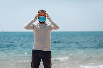 COVID-19 Pandemic Coronavirus man on the beach wearing face mask protective for spreading of Coronavirus Disease 2020 and touching his forehead. SARS-CoV-2 concept