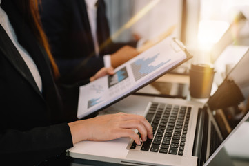 Businessman hand using laptop and tablet with social network diagram and two colleagues discussing data on desk as concept in morning light.