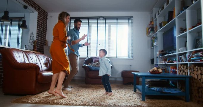 Family fun at home concept, happy young Caucasian father, mother and little son enjoy dancing together slow motion.