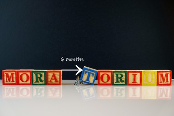 Conceptual of moratorium granted by banks during financial crisis. Miniature workers separating wooden cubes TORIUM from MORA over dark background. Texts 6 months visible. Focus on selective cubes . - obrazy, fototapety, plakaty