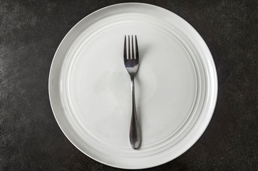 Fork on a white empty clean plate on a black background