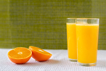 Orange juice in a glass with orange decoration, the best start to the day. Photo on a green background.