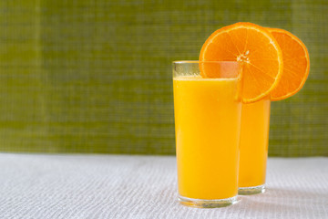 Orange juice in a glass with orange decoration, the best start to the day. Photo on a green background.