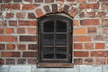 Antique wooden window with metal fittings and hinges in an old red brick wall of an ancient European castle.