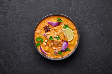 A Chicken Massaman Curry in black bowl at dark slate background. Massaman Curry is Thai Cuisine dish with chicken meat, potato, onion and many spices. Thai Food. Copy space. Top view - obrazy, fototapety, plakaty
