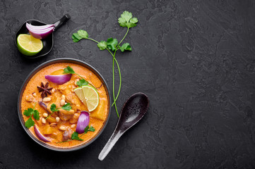 A Chicken Massaman Curry in black bowl at dark slate background. Massaman Curry is Thai Cuisine dish with chicken meat, potato, onion and many spices. Thai Food. Copy space. Top view