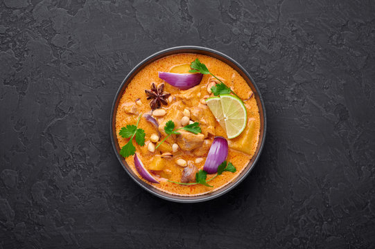 A Chicken Massaman Curry In Black Bowl At Dark Slate Background. Massaman Curry Is Thai Cuisine Dish With Chicken Meat, Potato, Onion And Many Spices. Thai Food. Copy Space. Top View