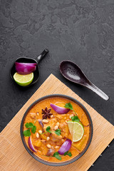 A Chicken Massaman Curry in black bowl at dark slate background. Massaman Curry is Thai Cuisine dish with chicken meat, potato, onion and many spices. Thai Food. Copy space. Top view