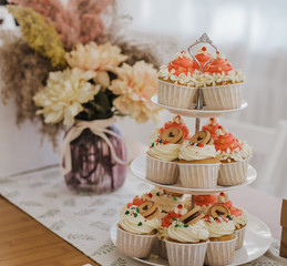 Stand with capcakes, white and pink buttercream. Blurred flowers at the background. Romantic pastels.