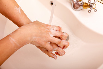 Young woman washing hands in modern sink with soap and lathering suds to protect against the coronavirus or covid 19. Bathroom hygiene concept.