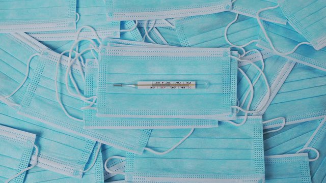 Nurse's hand in medical gloves puts a thermometer with a temperature of 38 on a background of medical masks.