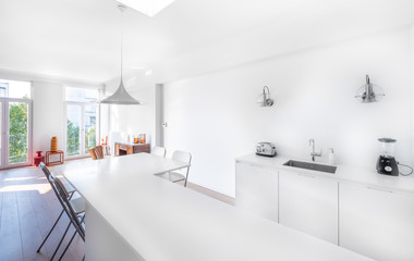 New stylish bright kitchen with white cabinets. Spacious modern interior with wooden floor, white table, industrial chairs and big ceiling window.