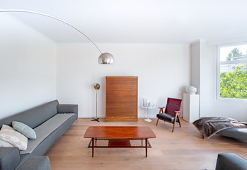 Minimal stylish bright living room with wood floor, big sofas, wooden table, modern lamp, big windows and retro furnitures. Spacious Scandinavian stylish interior with vintage decor