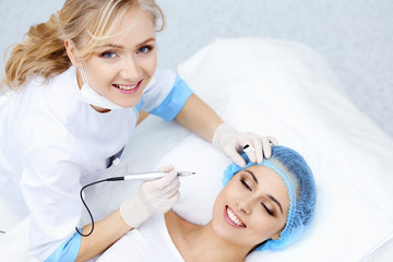 Naklejka premium Professional beautician doing eyebrow tattoo at woman face. Permanent brow makeup in beauty salon, closeup. Cosmetology treatment