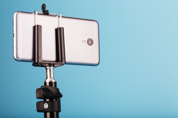 Smartphone on a tripod as a photo-video camera on a blue background. Record videos and photos for your blog.