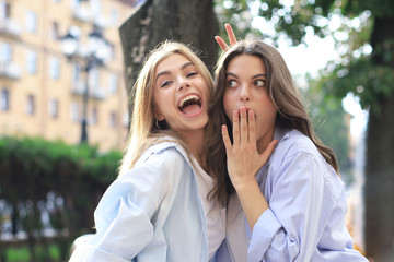 Fototapeta premium Two young smiling hipster women in summer clothes posing on street.Female showing positive face emotions.