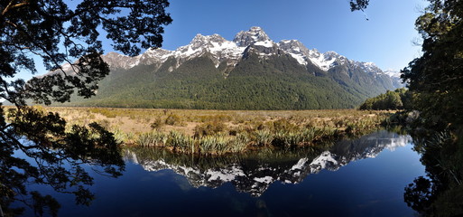 Panorama of snow capped mountains in New Zealand reflecting in Mirror Lake near Milford Sound