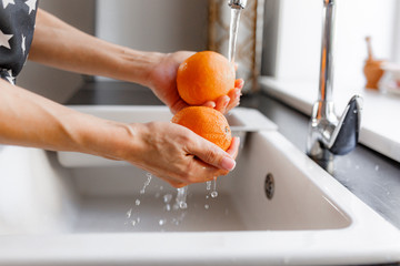 Hands of woman washing ripe orange under faucet in the sink kitchen