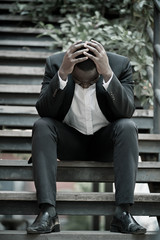 Serious African businessman professional failed or upset in his job and sitting on staircase. Business problem concept.